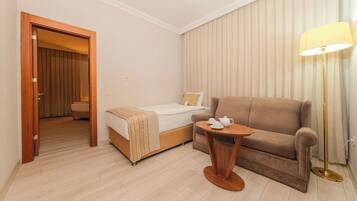 Habitación de hotel con cama, sofá, una mesita con lámpara y puerta que da a otra habitación.