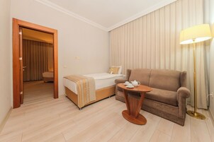 Habitación de hotel con cama, sofá, una mesita con lámpara y puerta que da a otra habitación.