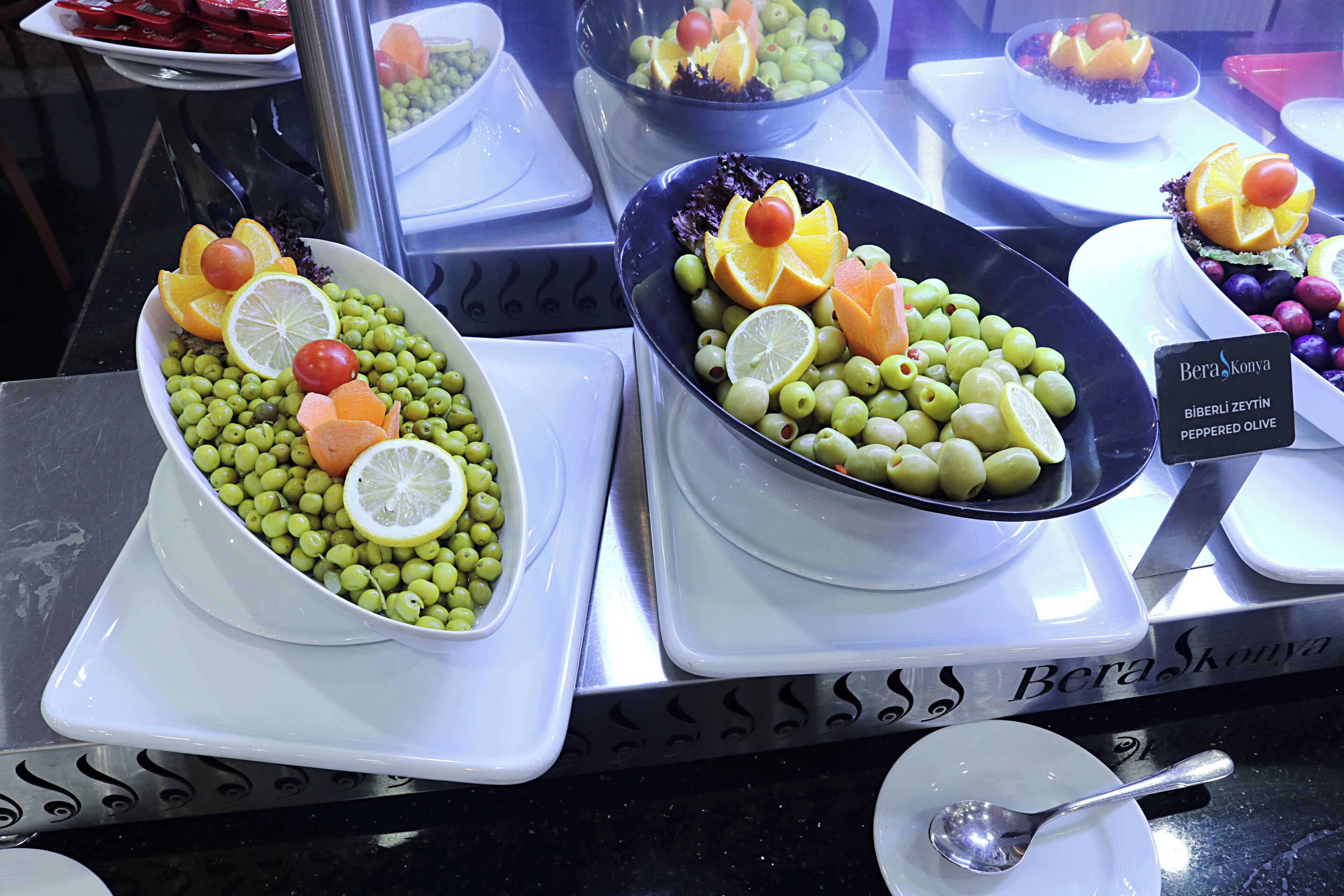 Two bowls of olives and citrus fruits on a counter.