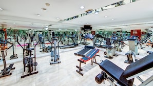 Un gimnasio moderno con diversas máquinas de ejercicio, espejos y suelo de madera.