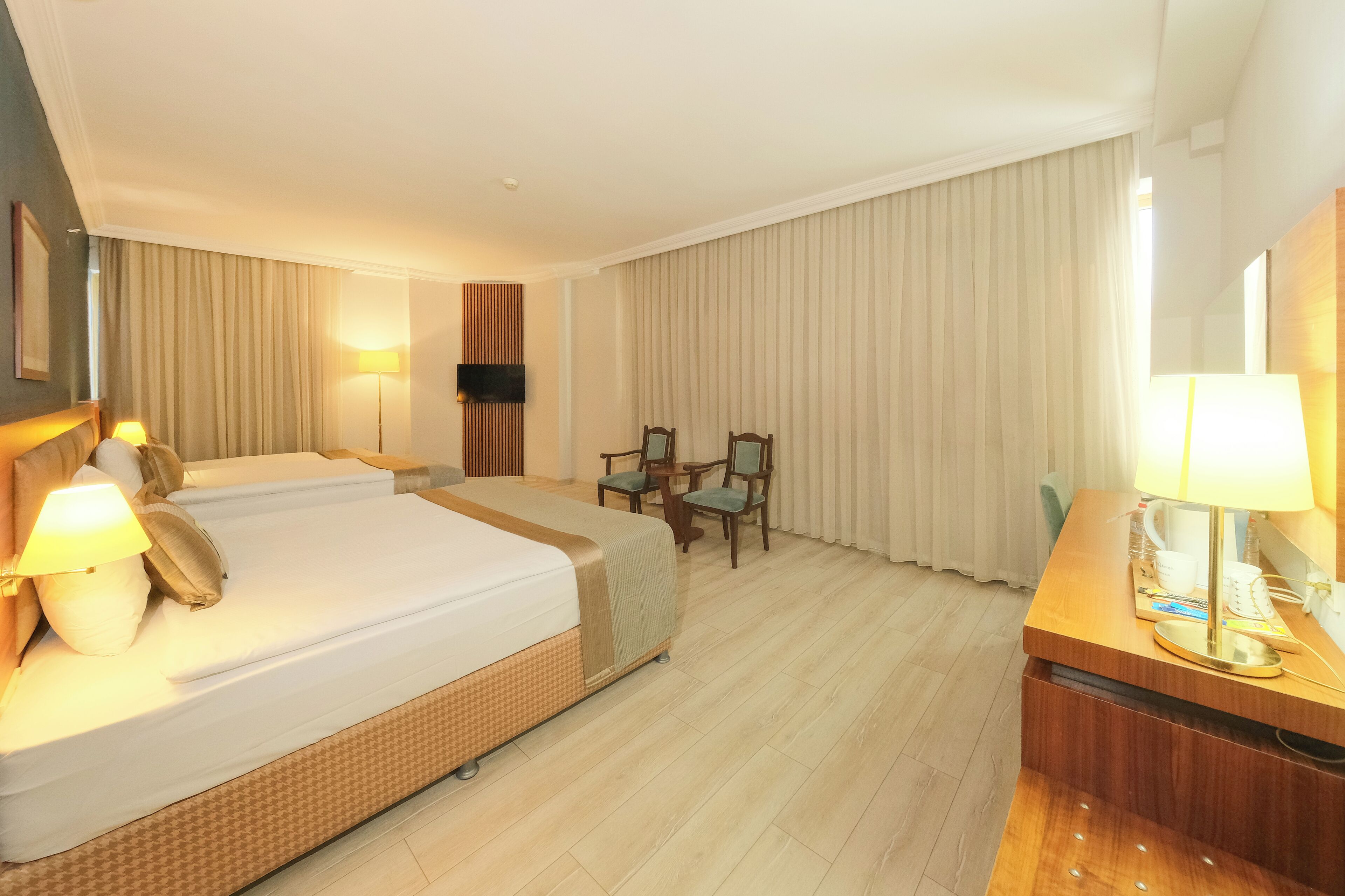 Habitación de hotel con cama, lámparas de noche, un escritorio con lámpara, una silla y televisor en la pared.