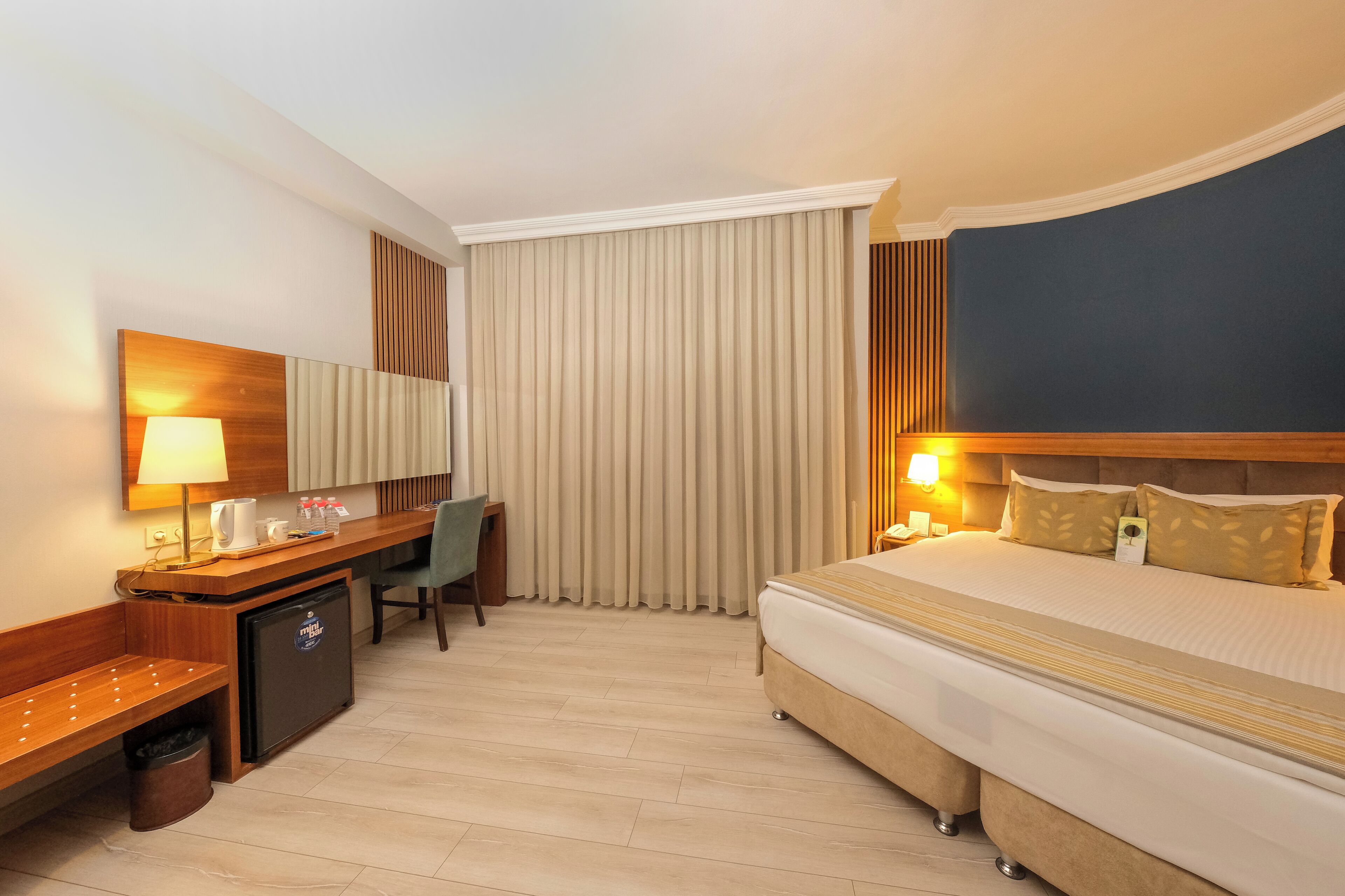 A hotel room with a bed, desk, chair, and a small refrigerator.