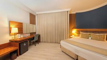 Una habitación de hotel con cama, escritorio, silla y un refrigerador pequeño.