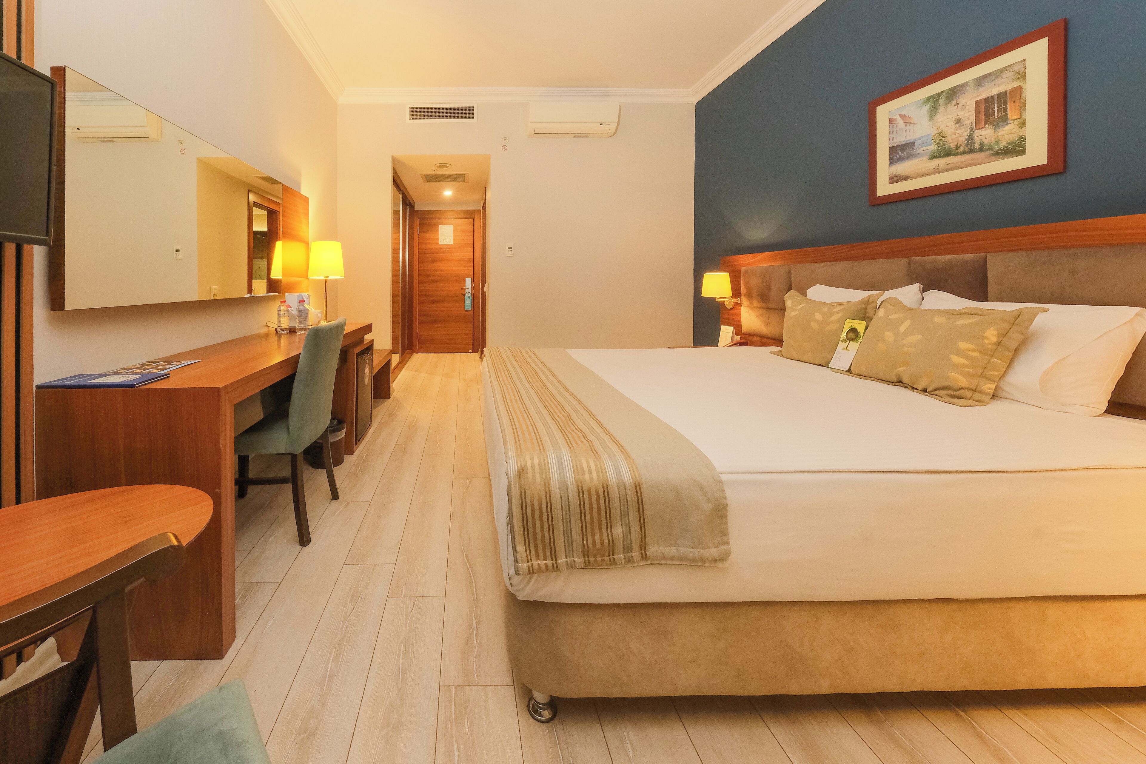 Una habitación de hotel con cama, escritorio, silla y un espejo grande.