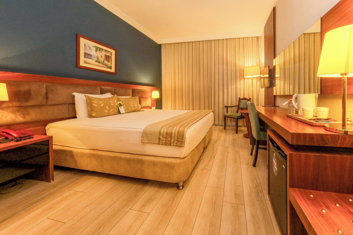 Una habitación de hotel con cama, mesita de noche, lámpara, escritorio, silla y televisor.