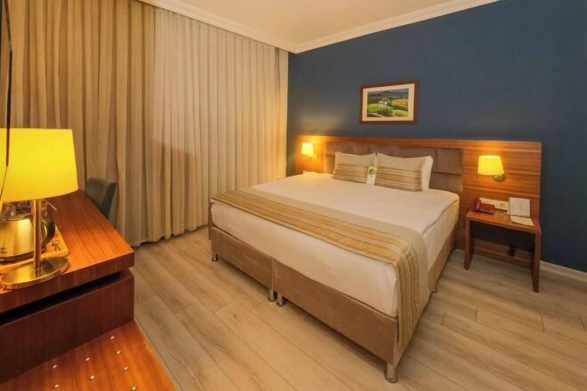 Una habitación de hotel con una cama, mesitas de noche, una lámpara y un cuadro en la pared.