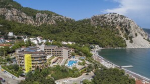 Um hotel à beira-mar com piscina, acesso à praia e montanhas ao fundo.