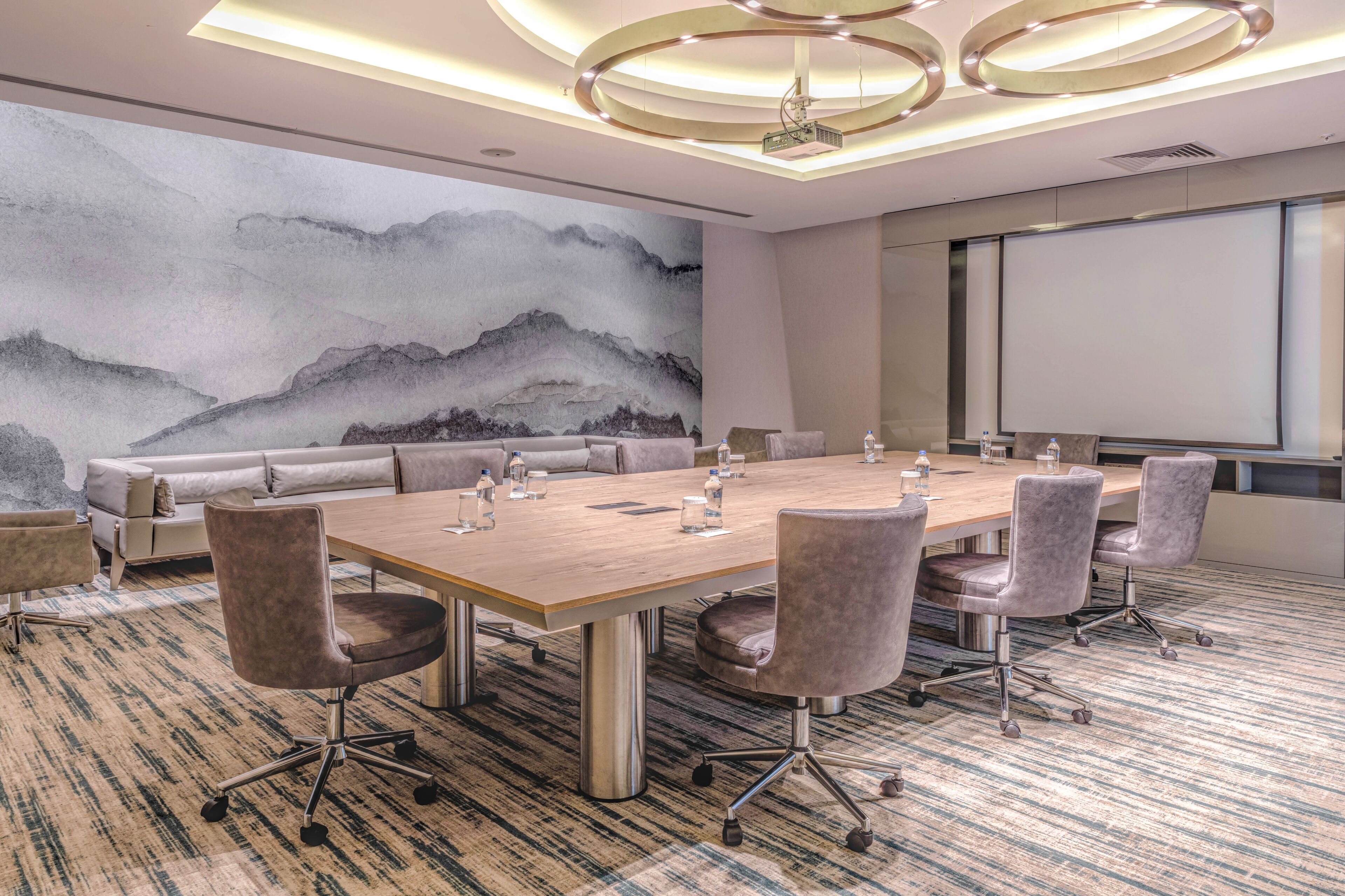 A conference room with a large table, chairs, a sofa, and a projector screen.