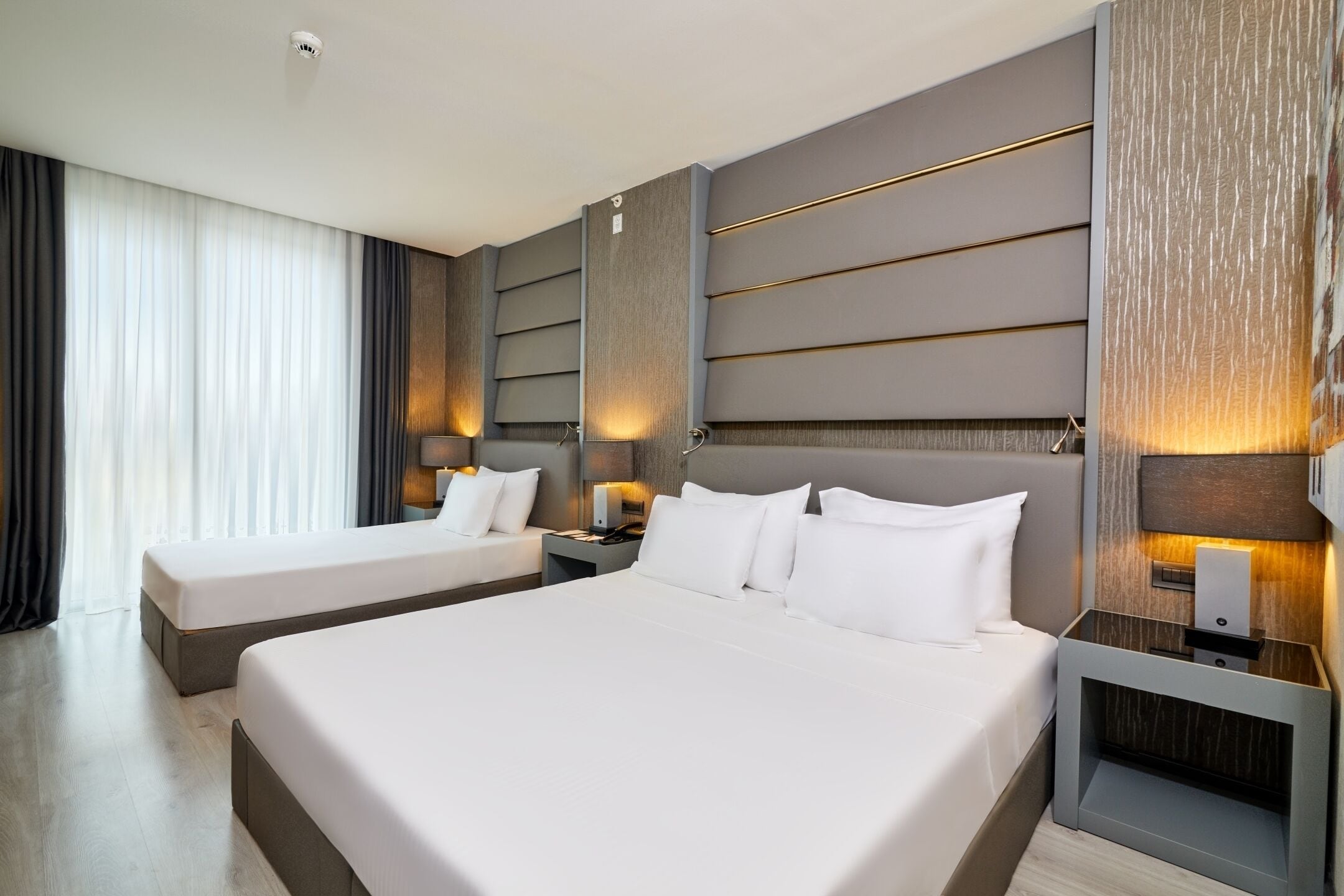 A hotel room with a large bed, two bedside tables, and a headboard with integrated lighting.