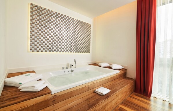 A modern bathroom with a large freestanding bathtub, wooden flooring, and a patterned wall above the sink.