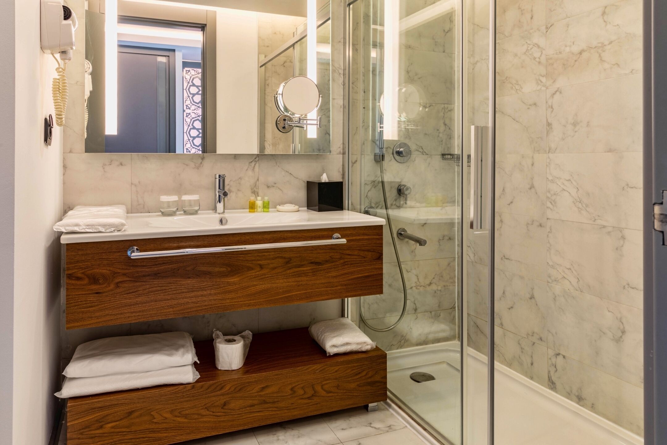 Un baño moderno con tocador de madera, cabina de ducha de vidrio y paredes de mármol.