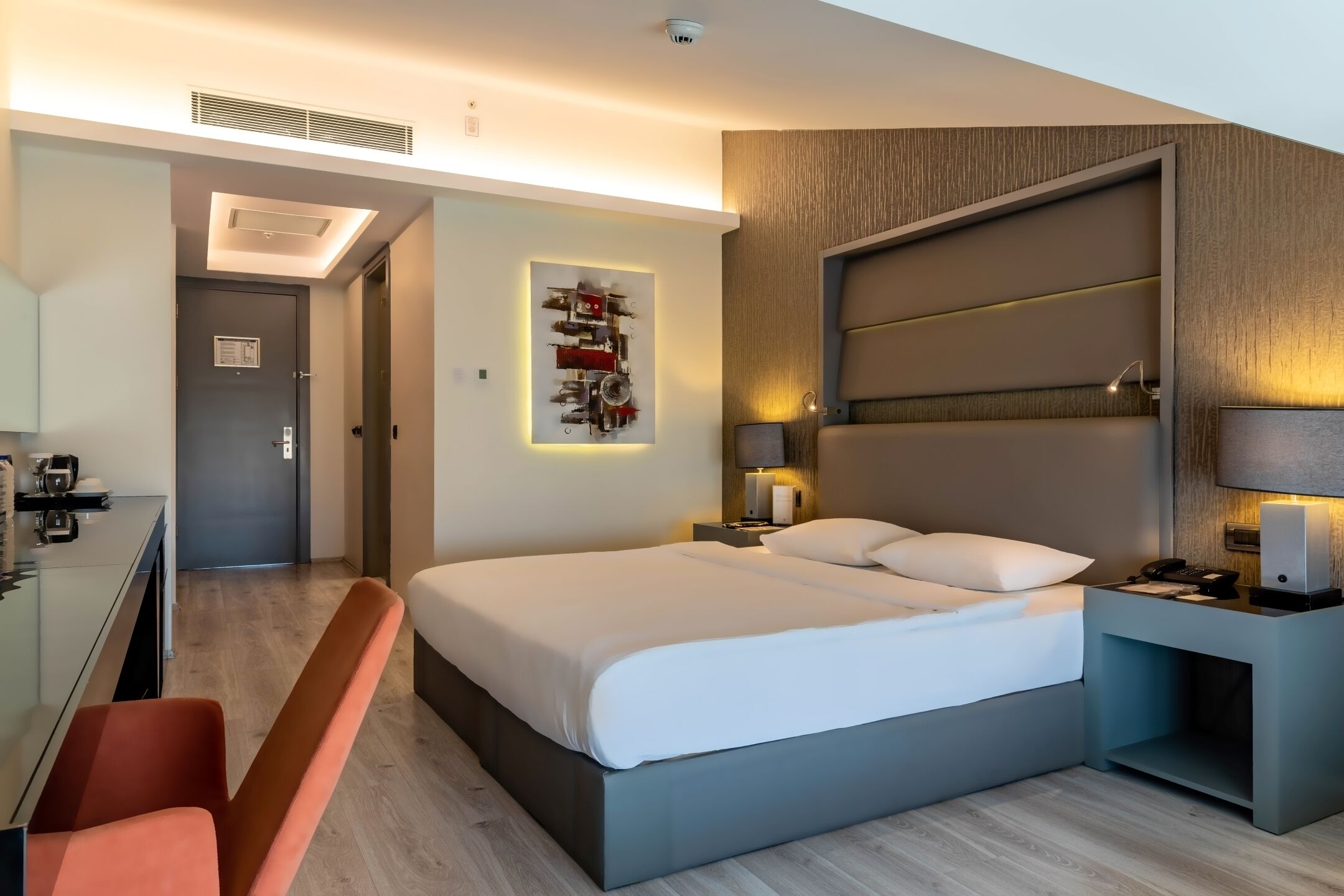 A modern hotel room with a large bed, bedside tables, a desk, and a chair.