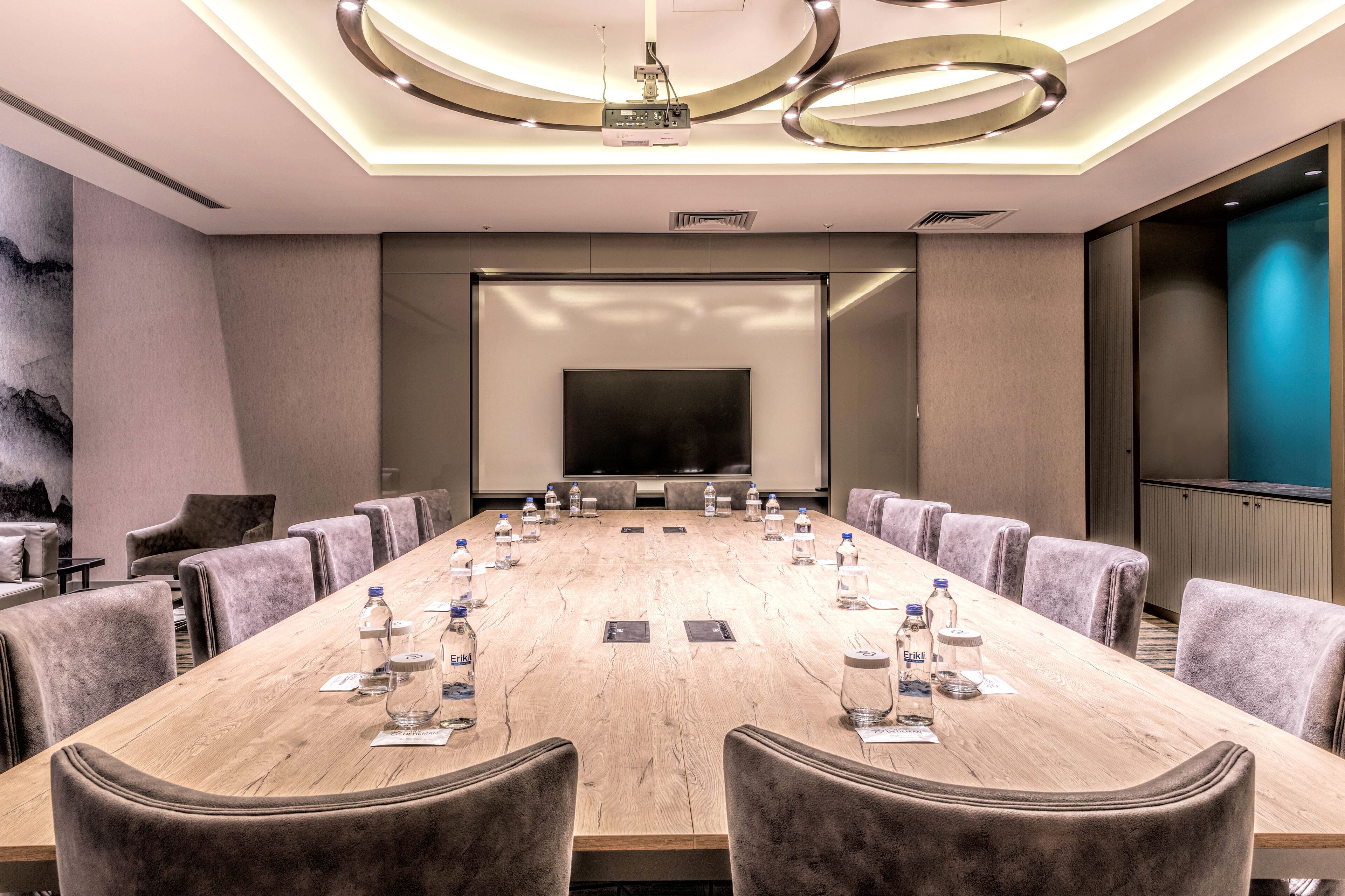 A conference room with a long table, comfortable chairs, water bottles, and a large screen.