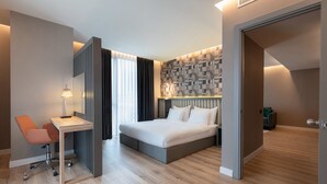 Habitación de hotel moderna con cama, escritorio y silla, destacando un cabecero de estampado geométrico y suelo de madera.