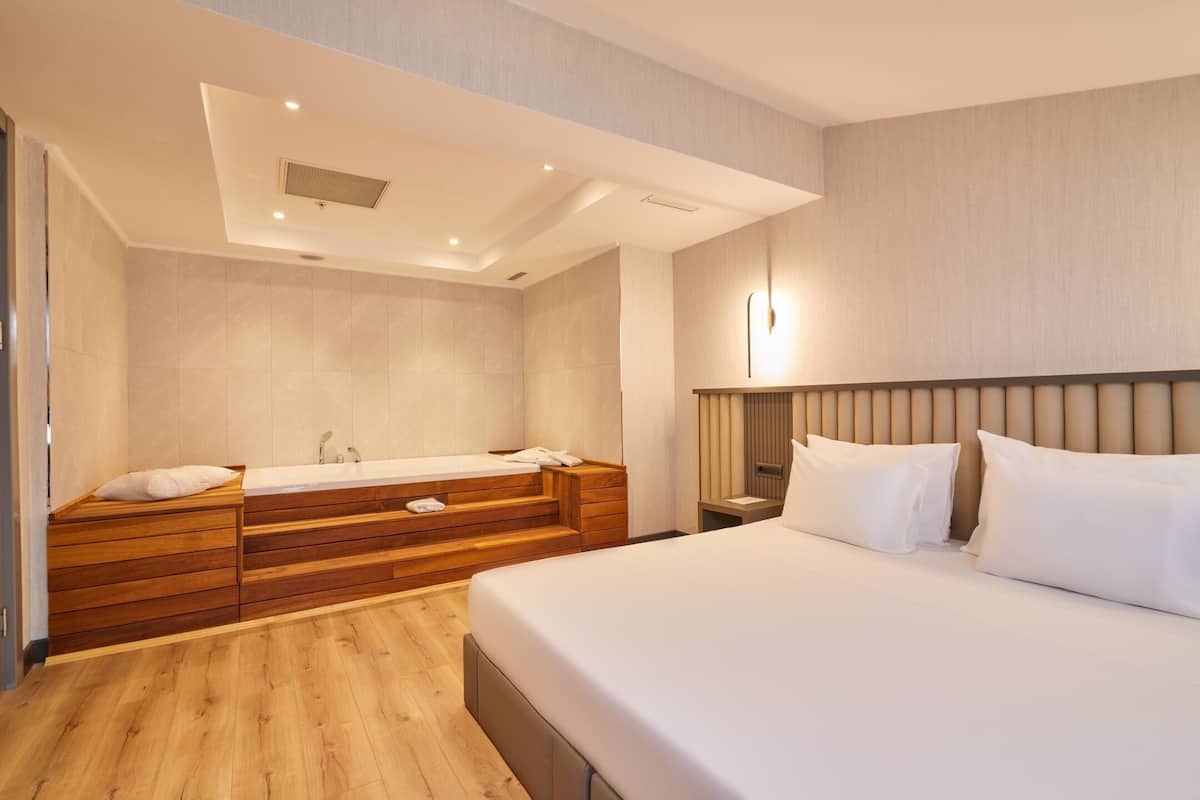 Una habitación de hotel moderna con una cama grande, tocador de madera y zona de ducha integrada.
