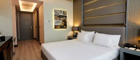 Una habitación de hotel moderna con una cama grande, una mesita de noche, una lámpara y un cuadro en la pared, además de un pasillo que conduce a otra habitación.