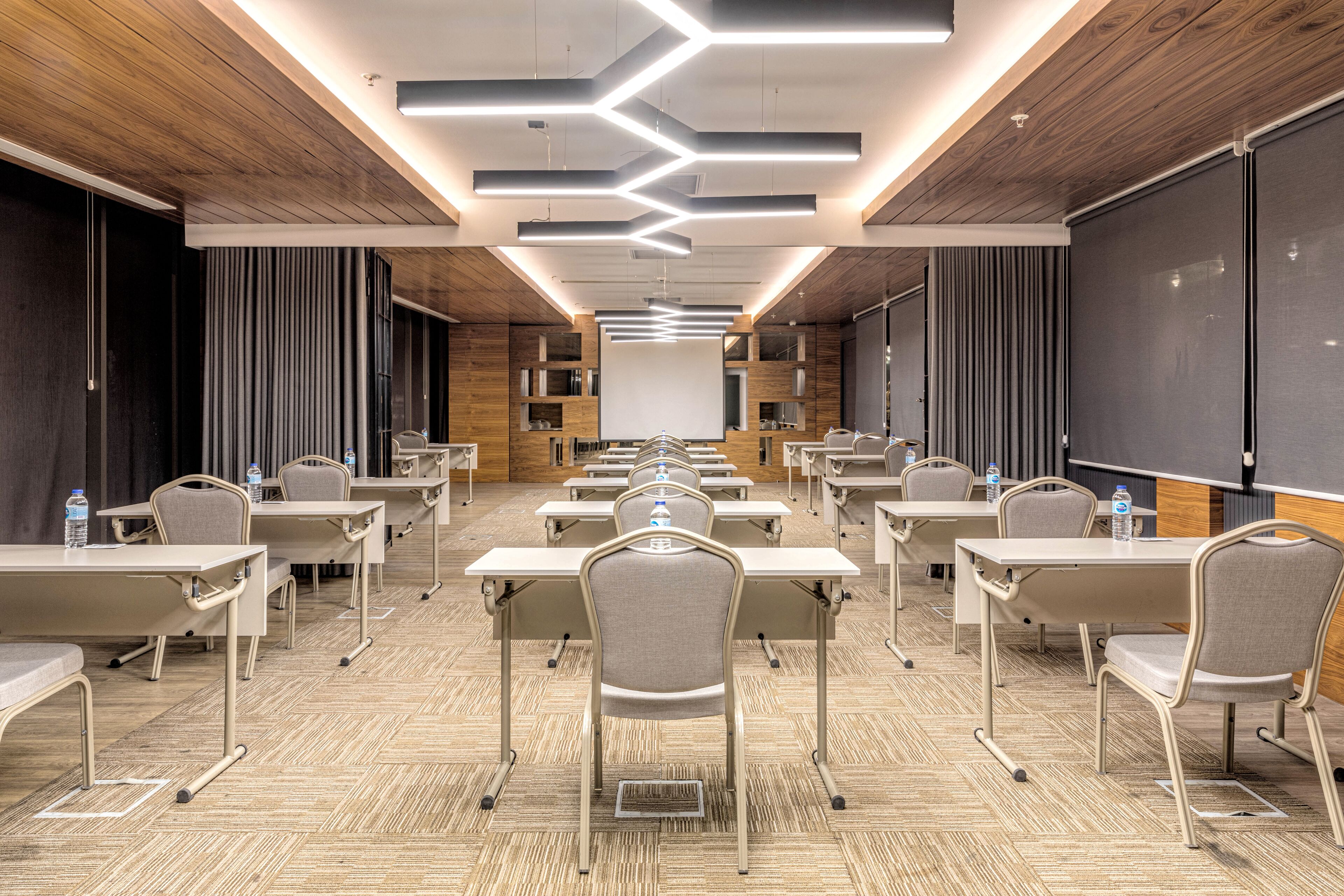 A conference room with rows of tables and chairs, a large screen, and a wooden ceiling.