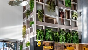 Un interior moderno con una zona de estar central, un jard ín vertical en la pared y un cartel que muestra opciones de comida y bebida.