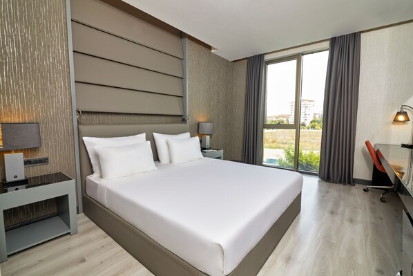 Une chambre d’hôtel moderne avec un grand lit, un bureau et une vue sur l’extérieur.