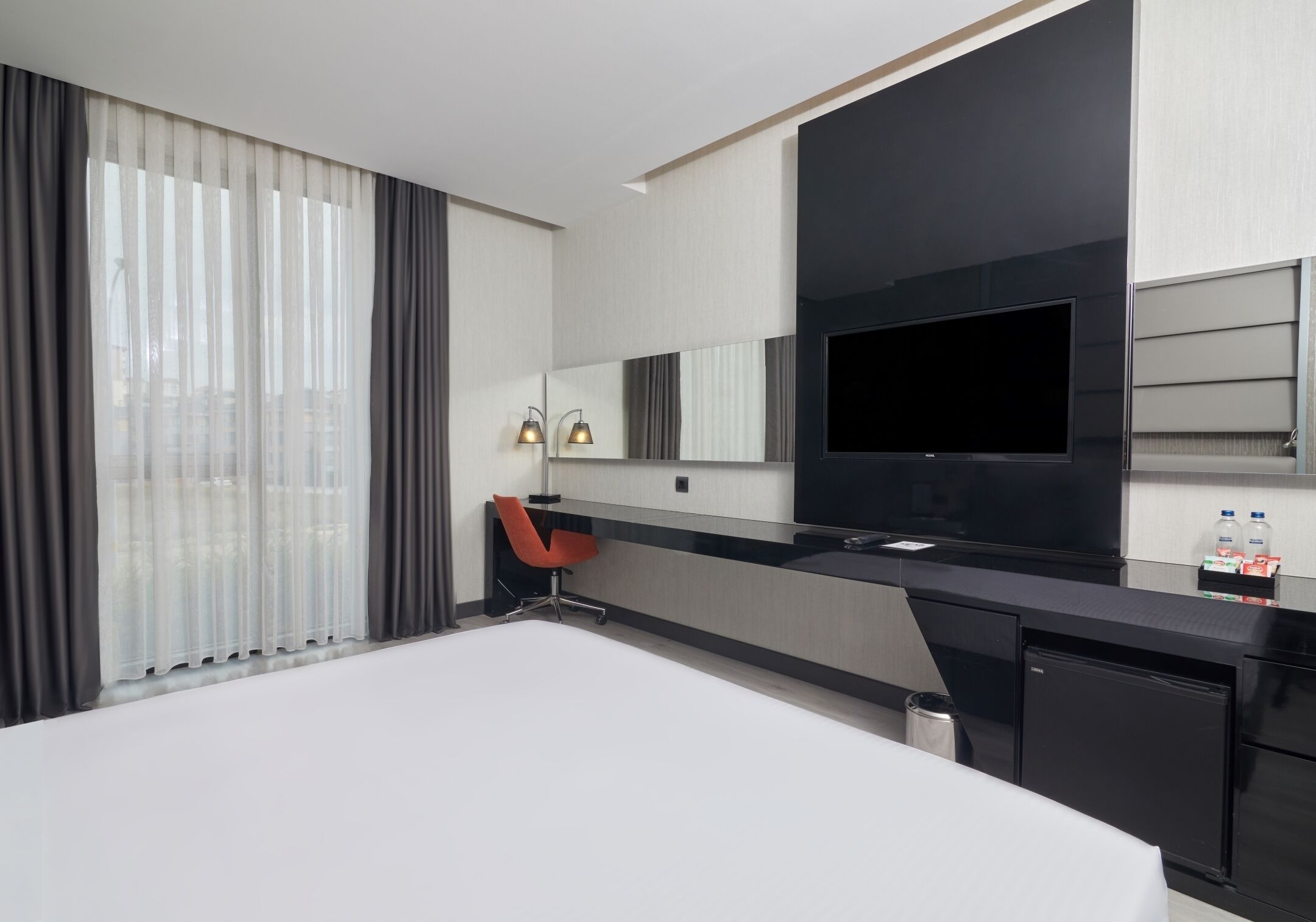 Habitació d'hotel moderna amb un llit gran, una taula de treball amb cadira, televisió de pantalla plana i un minibar.