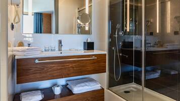 Un baño moderno con tocador de madera, un espejo grande, cabina de ducha de vidrio y un teléfono en la pared.