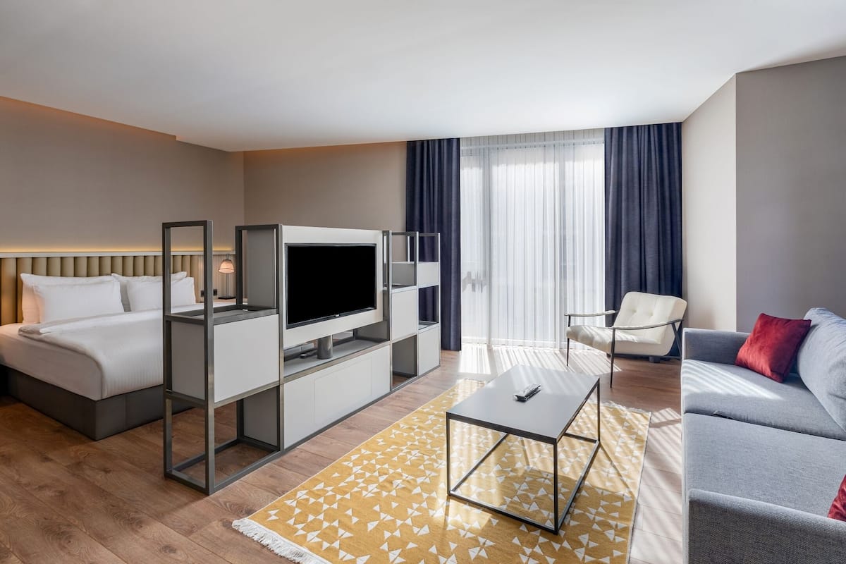 Una habitación de hotel moderna con cama, televisor, sofá y mesa de comedor.
