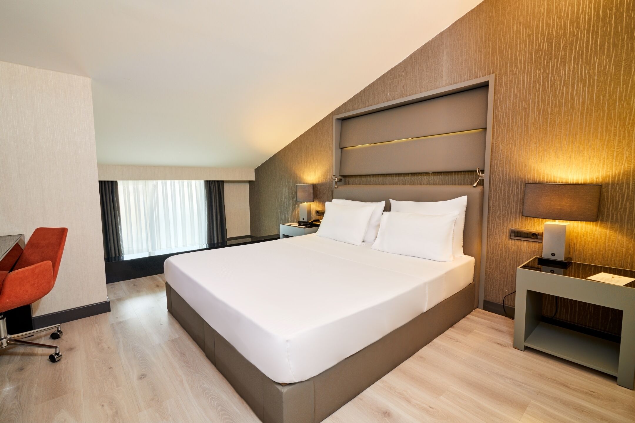A modern hotel room with a large bed, a desk, and a chair.