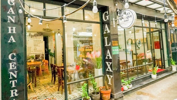 A hotel entrance with a reception desk, potted plants, and a sign reading "GALAXY Hotel".