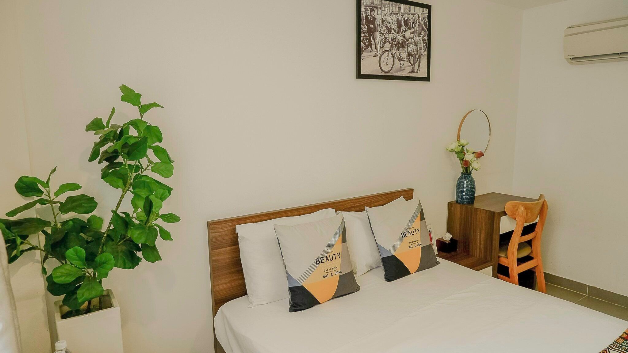 Une chambre d’hôtel bien rangée, avec un lit, un bureau, une chaise et une plante en pot.