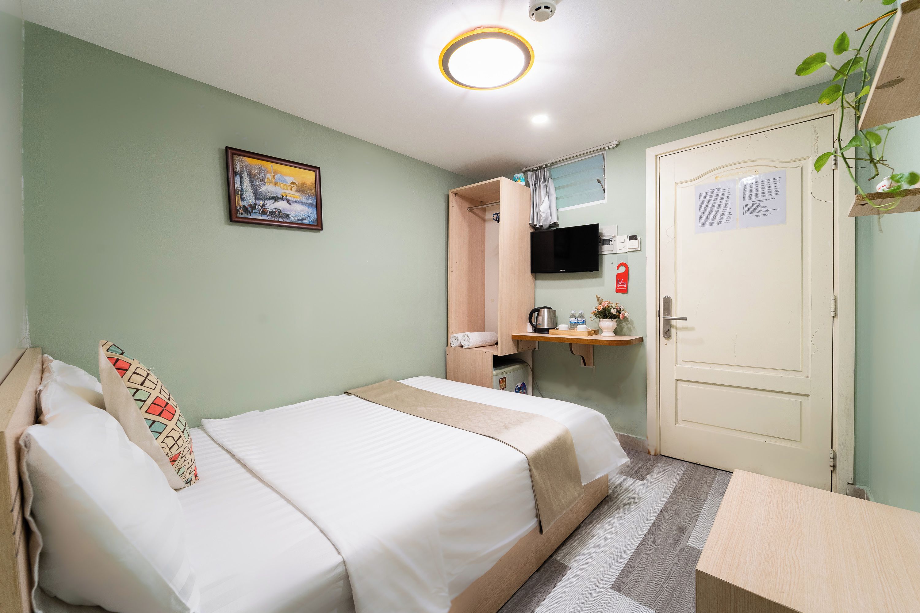 A hotel room with two beds, a television, a small table, and a door with a sign.