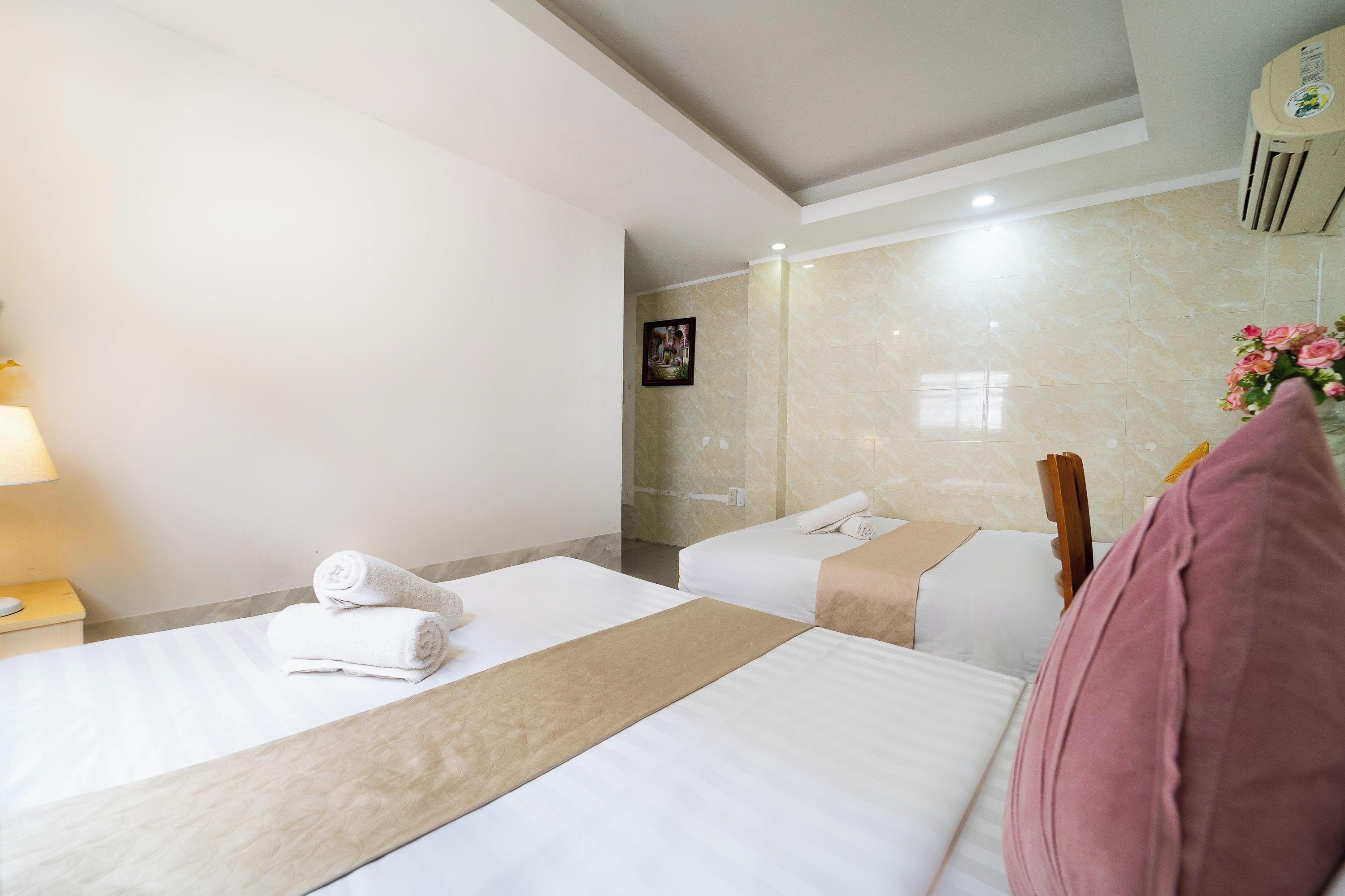 Een hotelkamer met twee bedden, een nachtkastje, een lamp, een spiegel, een foto aan de muur en een bloemenboeket.