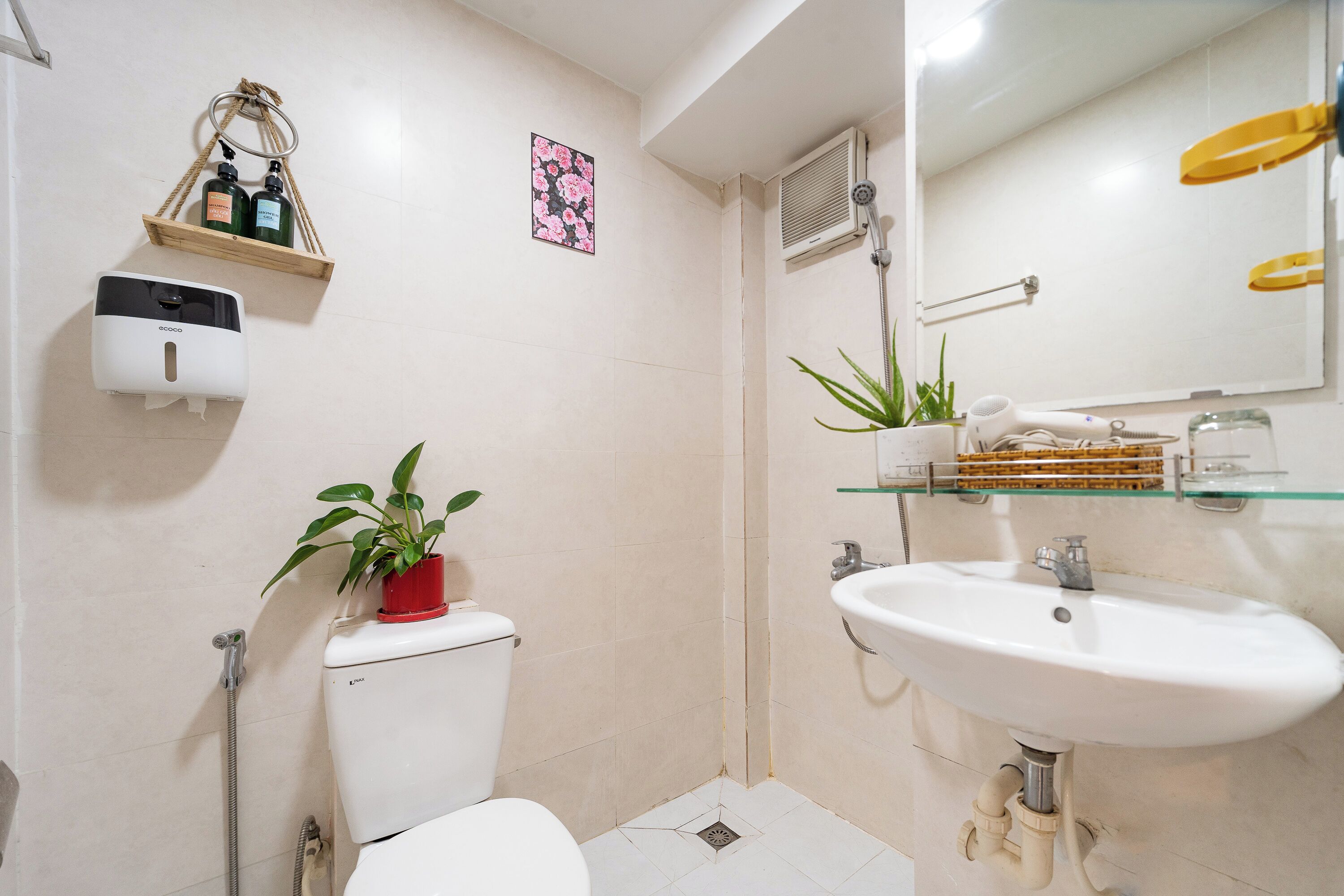 Une salle de bain équipée de toilettes, d’un lavabo, d’une douche et d’un distributeur de savon mural.
