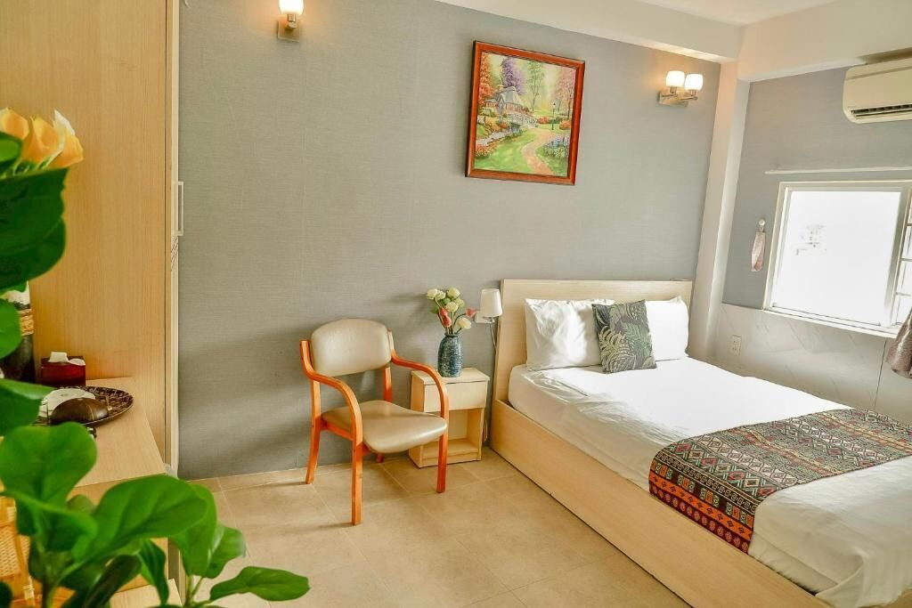 A bedroom with a bed, a chair, a nightstand, a painting, and a window with an air conditioner.