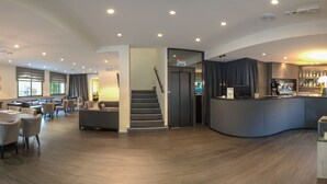 Um lobby moderno de hotel com balcão de recepção, área de estar e escadaria.