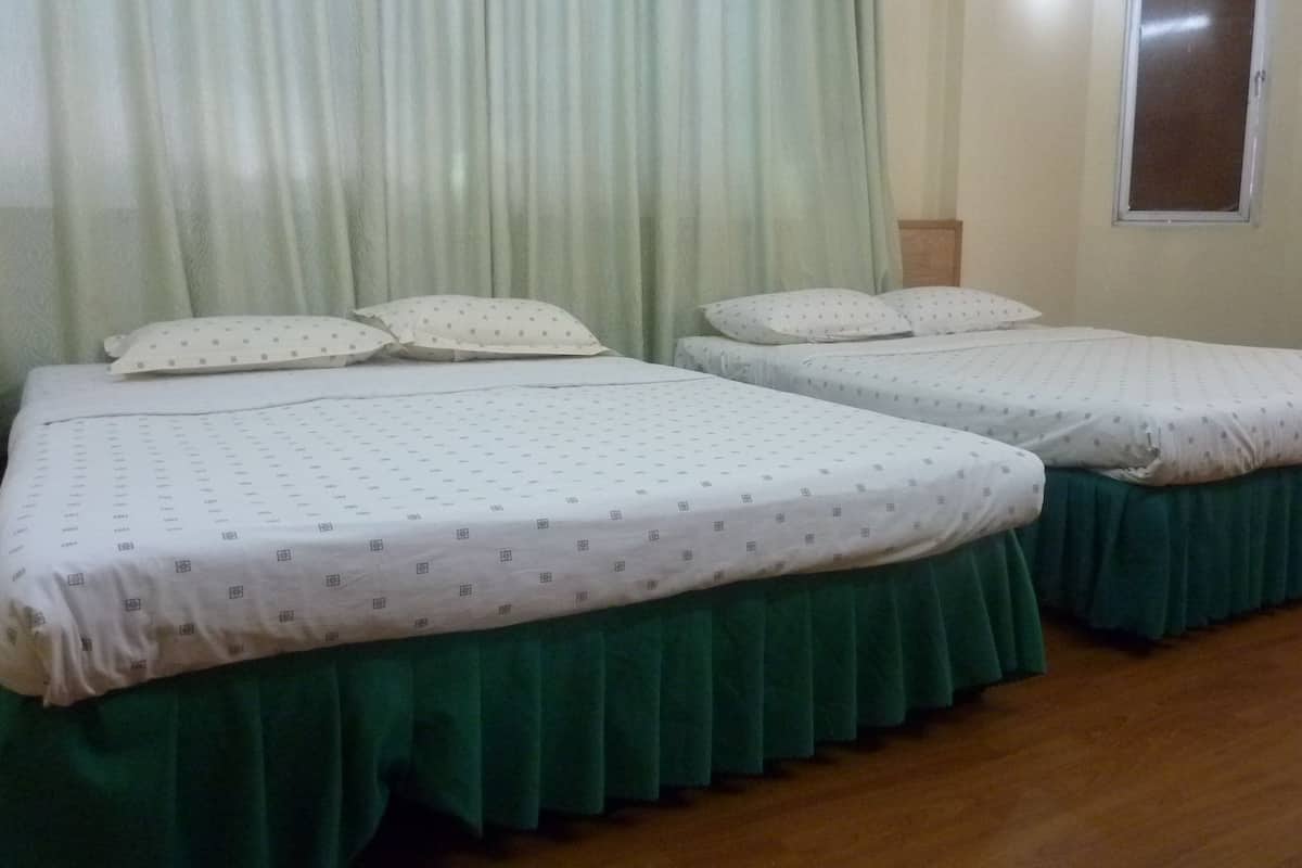 A room with two beds, each with a green skirted bedspread and white bedding with a subtle pattern.