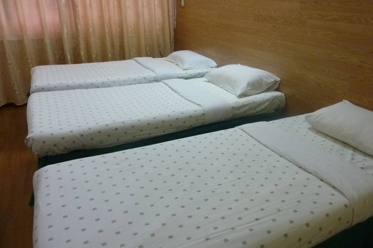 A room with three beds, each with a white mattress and matching pillow, and a wooden headboard.