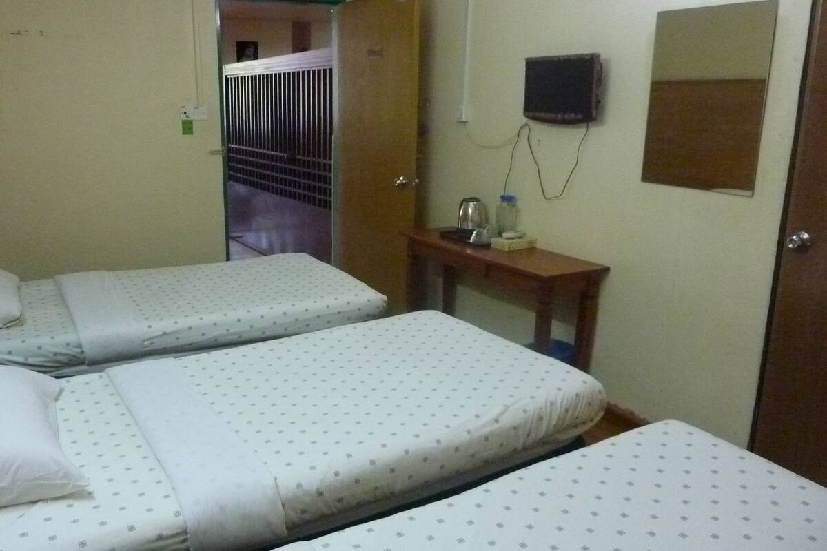 A hotel room with two beds, a small table with a kettle, a mirror, and a TV on the wall.
