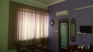 Una habitación con una mesa de comedor, sillas, un equipo de aire acondicionado, una puerta y una pequeña mesa con tetera y tazas.