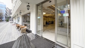 En hotellentrél med en glasdörr, ett utomhusområde med sittplatser och utsikt in i hotellets interiör.