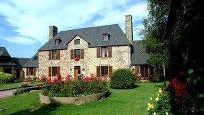 Un bâtiment en pierre doté d’un toit en pente, de nombreuses fenêtres et d’un jardin bien entretenu, agrémenté de fleurs.