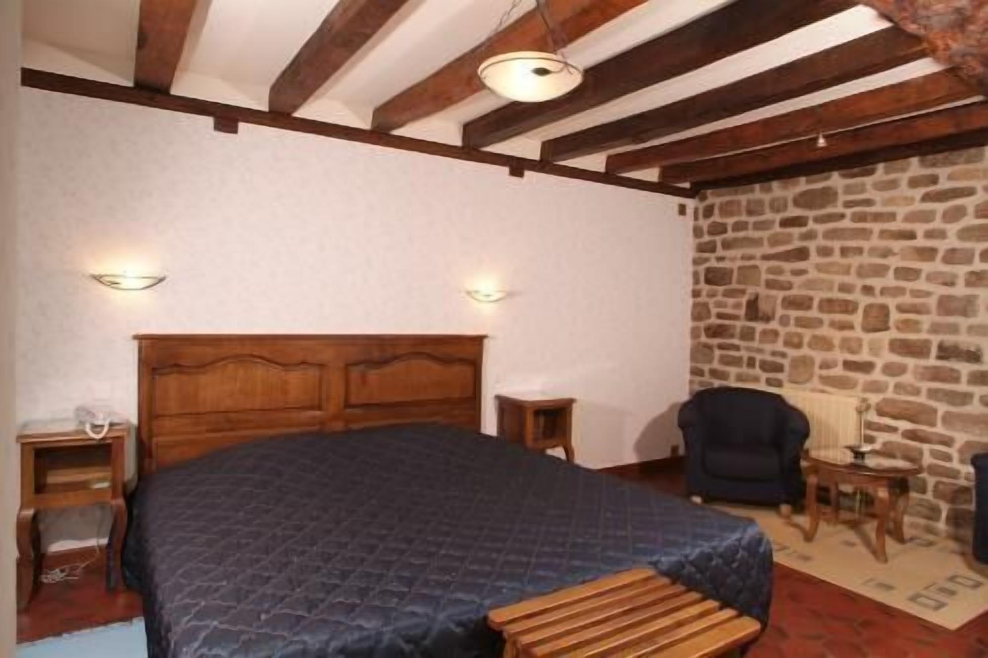 Une chambre à coucher avec un lit en bois, deux tables de chevet, un mur en pierre et un plafond avec des poutres apparentes.