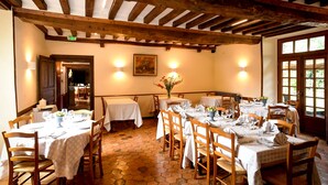 Un restaurant doté d’un sol carrelé à motifs hexagonaux, de poutres en bois au plafond, et de tables recouvertes de nappes blanches, accompagnées de chaises.