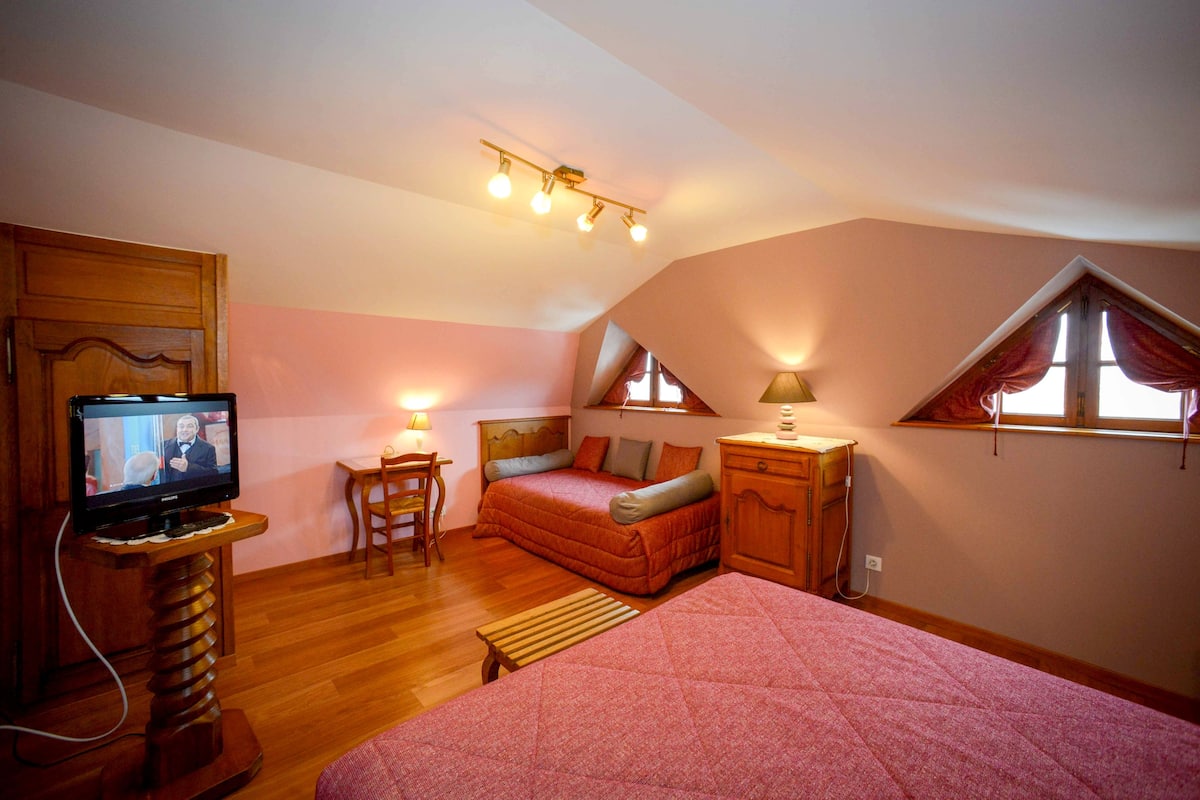 Une chambre à coucher comprenant un lit, un bureau, une chaise, un téléviseur et une fenêtre avec des rideaux.