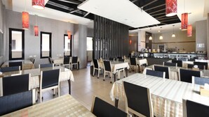 Un restaurant moderne avec des tables en verre, des chaises noires et des lampes suspendues rouges.