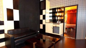 Un salon moderne avec un canapé en cuir noir, une table basse en verre et un coin cuisine doté d’un pare-feu décoratif.