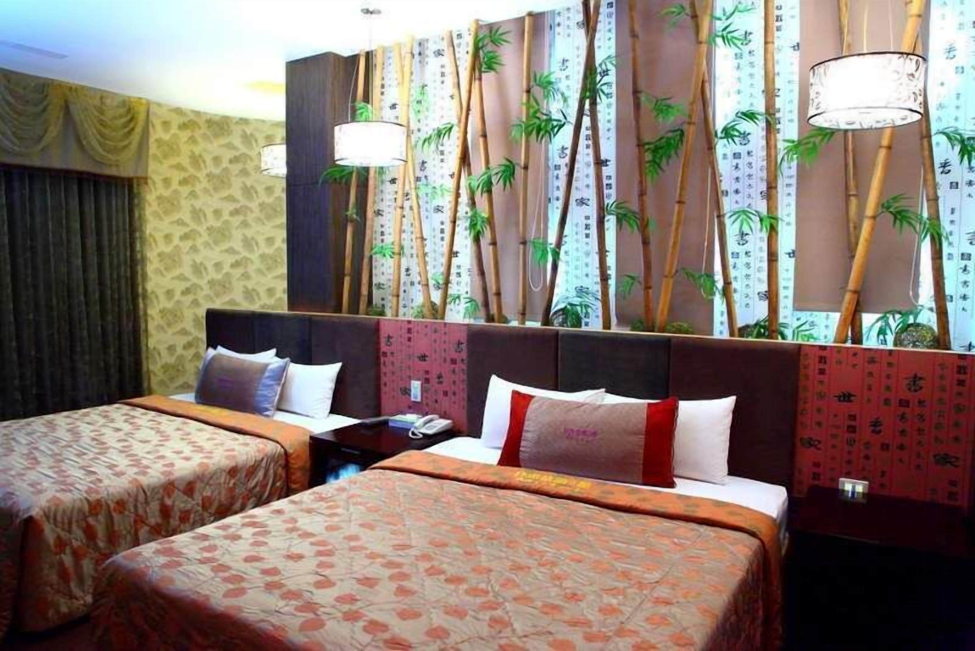 Habitación de hotel con dos camas, una pared grande con papel tapiz de bambú y una mesita de noche con una lámpara.