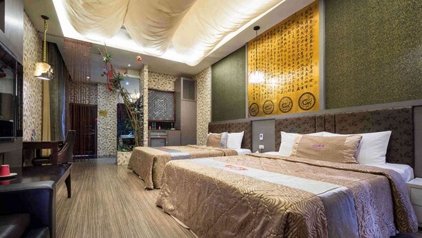 Une chambre d’hôtel avec deux lits, un bureau et un mur décoratif orné de calligraphies.