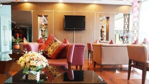 A modern hotel lobby with a sofa set, a flat-screen TV, and a vase of flowers on a glass table. - Noppakao Place (Chiang Mai)