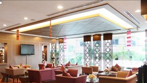 A spacious lobby with multiple seating areas, a flat-screen TV mounted on the wall, and large windows with decorative vertical panels. - Noppakao Place (Chiang Mai)