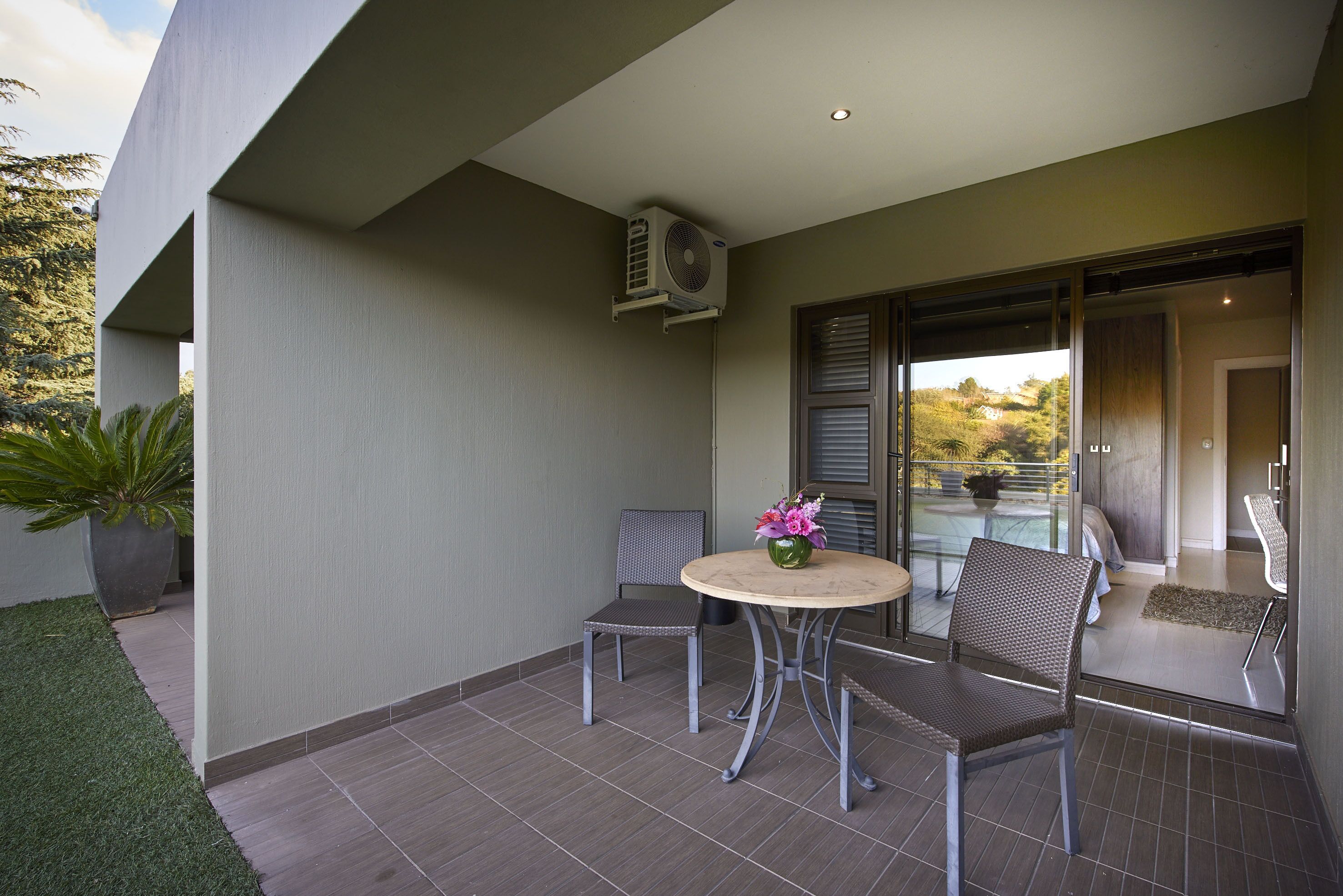 Un patio con una mesa redonda y dos sillas, una planta en maceta y vistas a una zona residencial.
